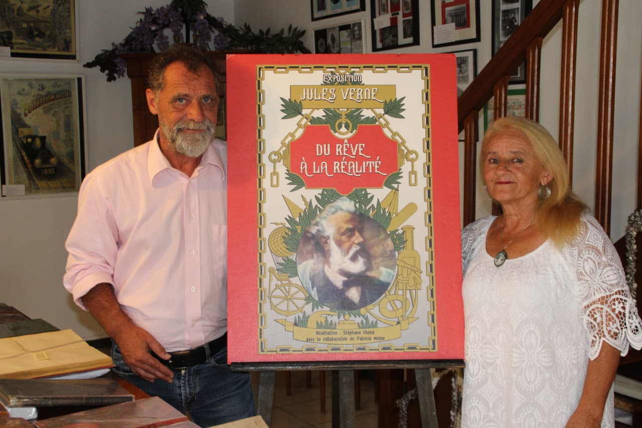 Un homme et une femme entourent l'affiche d'une exposition dédiée à Jules Verne